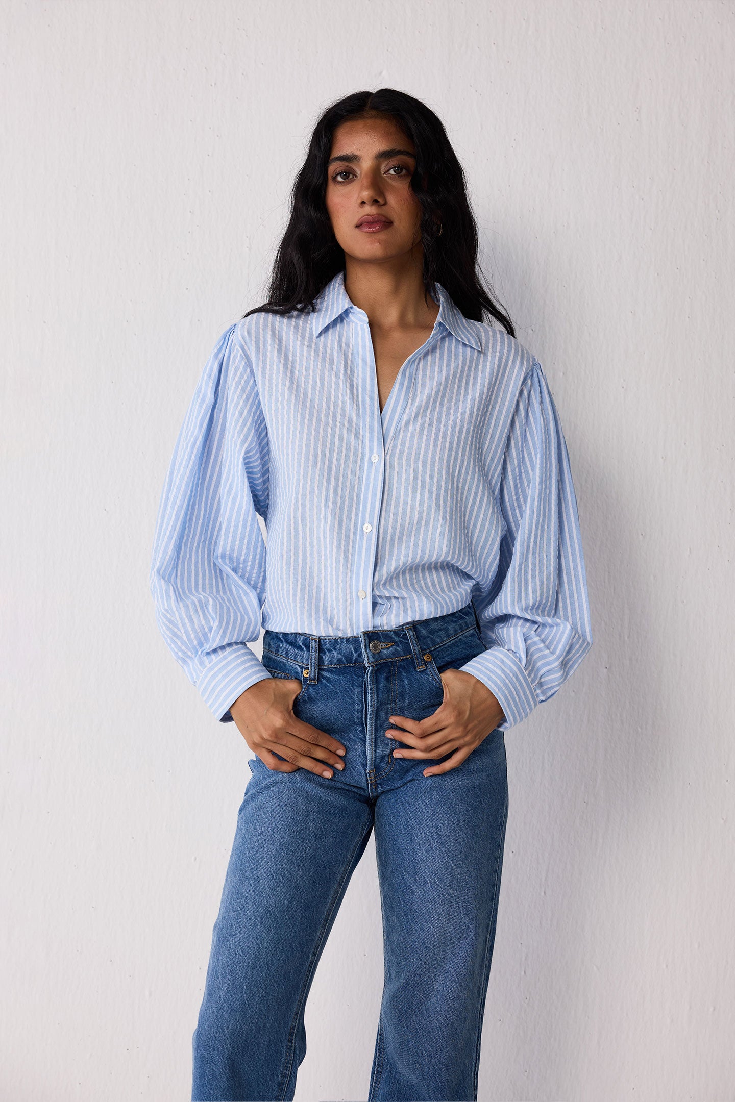 Woman wearing a light blue striped shirt and jeans against a plain background