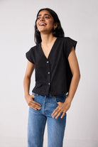 Woman wearing a black top and blue jeans against a plain background