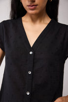 Black blouse with button details worn by a person on a plain background