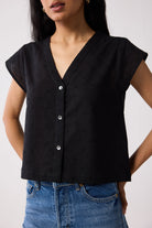 A woman wearing a black top with buttons and blue jeans on a white background