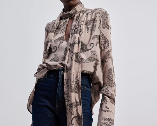 Person wearing a patterned scarf and dark jeans on a light gray background