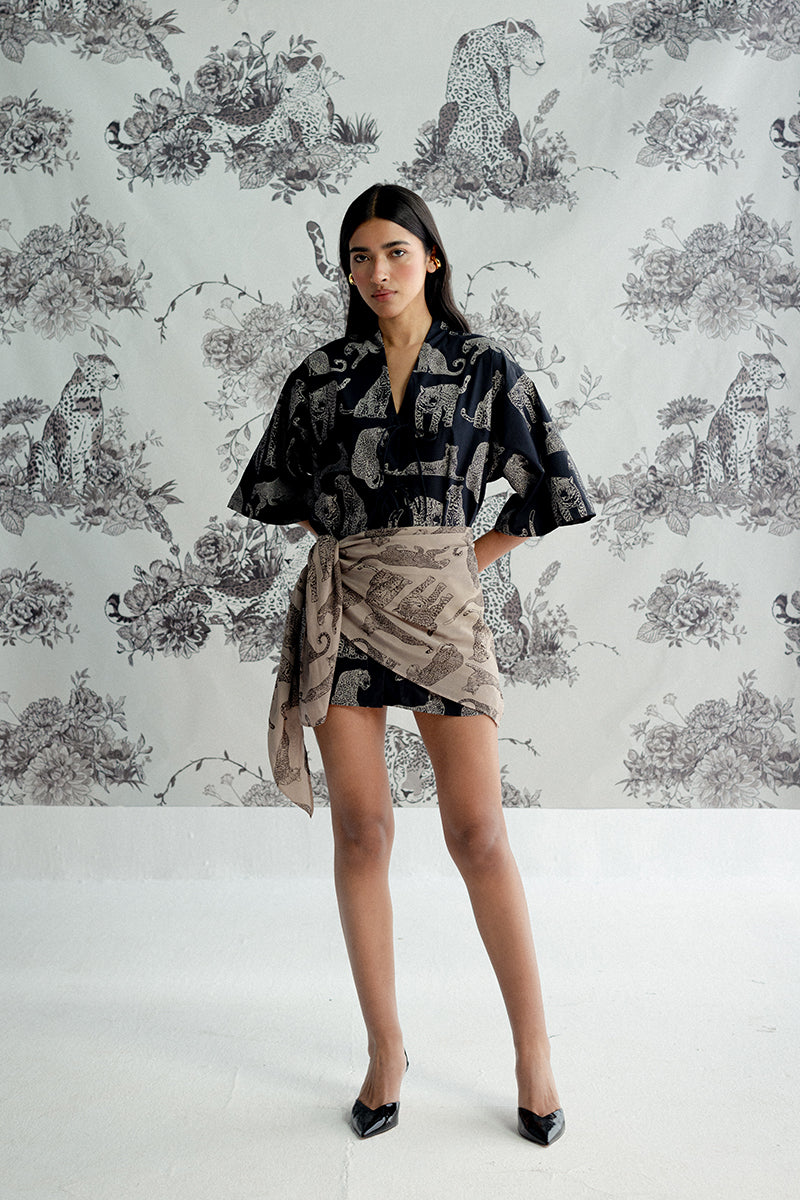Woman wearing a patterned kimono-style garment against a decorative wallpaper background