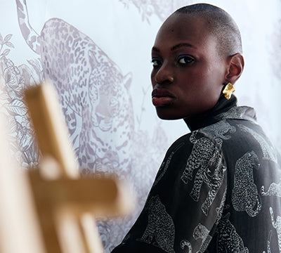 Woman in a patterned outfit standing next to an easel with a blurred background