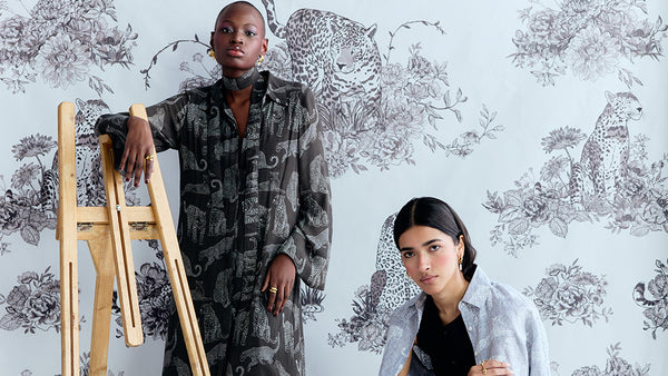 Two people standing against a floral-patterned wall with a wooden easel.
