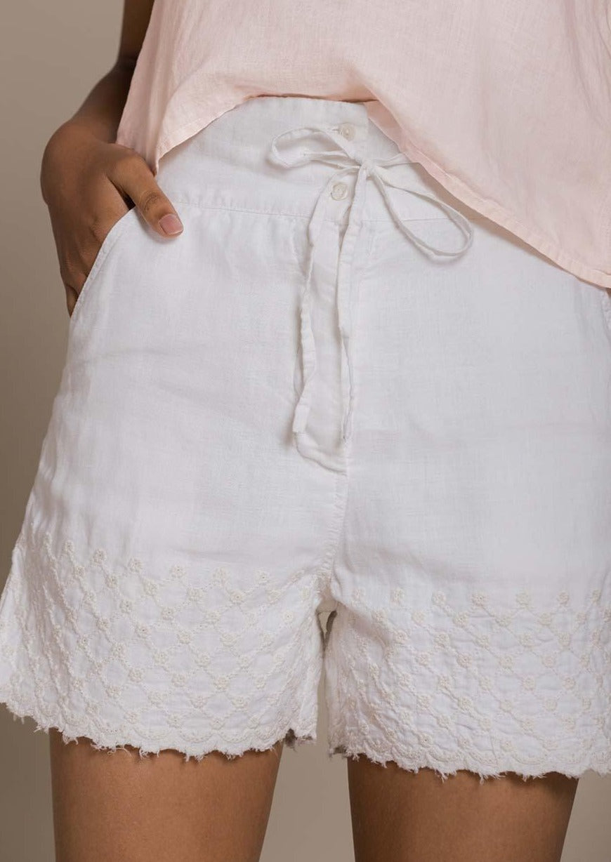 white beach shorts with embroidered borders and a drawstring at the waist.