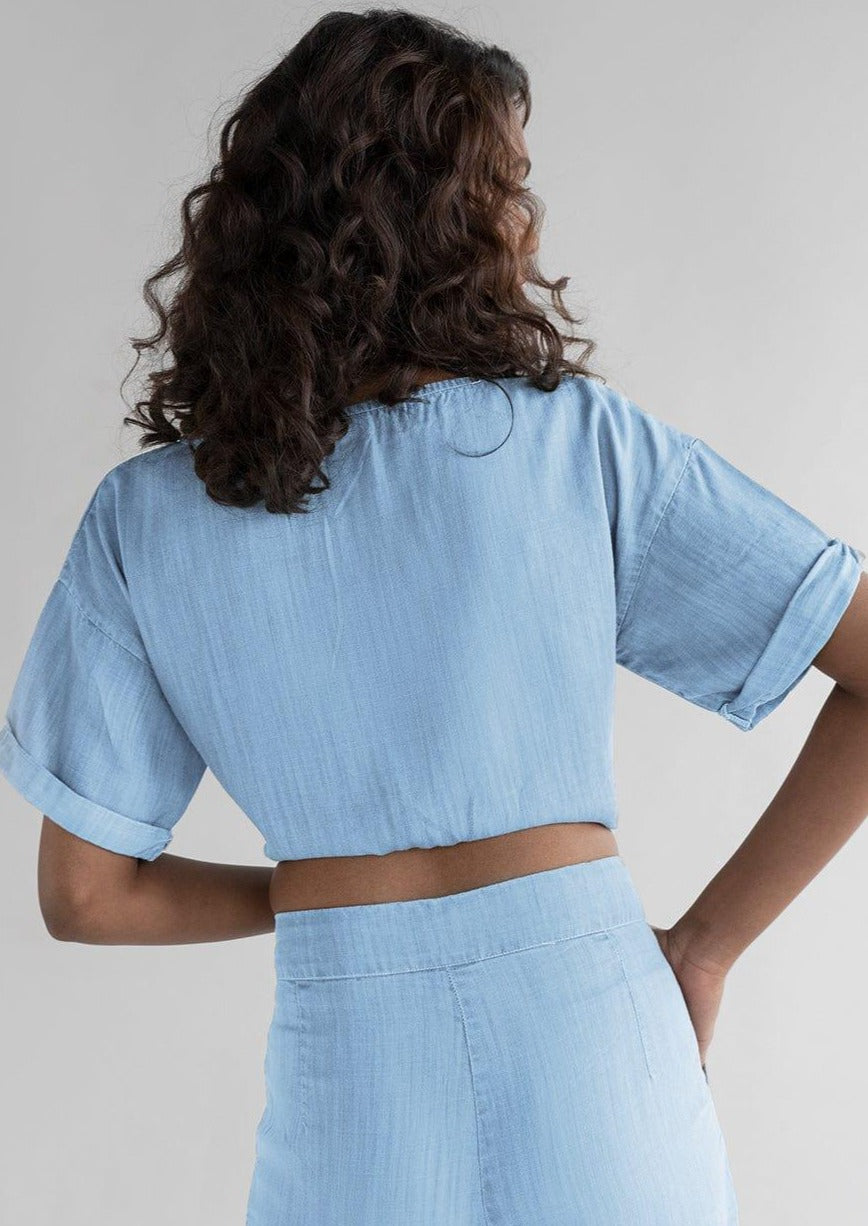 Back view of Twist and Sway Top in Blue by Reistor, featuring a relaxed cropped silhouette, rolled short sleeves, breathable fabric, and effortless everyday style.