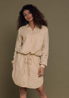 Beige mid length shirt dress with an oversized pocket in the front and a drawstring to tighten the waist.