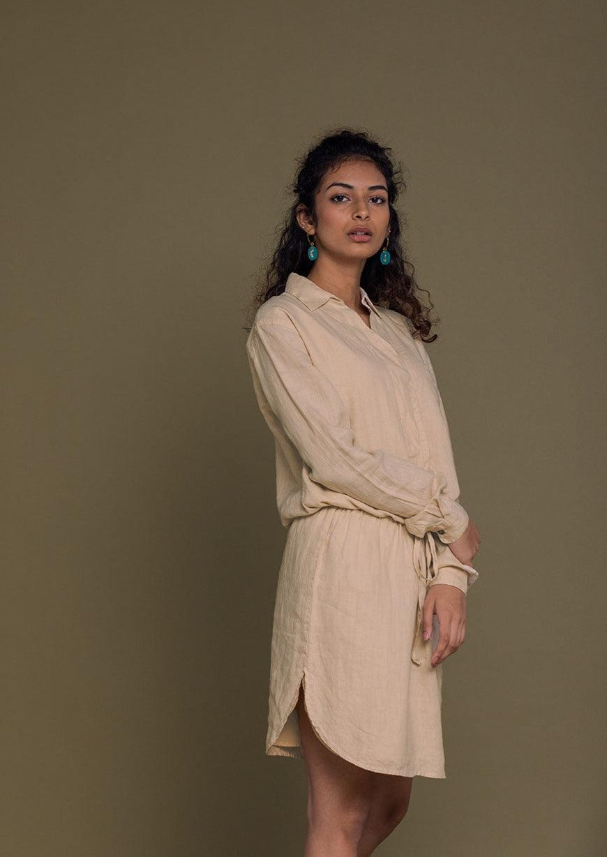 Beige mid length shirt dress with an oversized pocket in the front and a drawstring to tighten the waist.