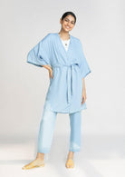 Model wearing the Reistor Wrapped in Happiness Overlay in Ocean Blue, showcasing a tie-waist design, airy fabric and a flowing contemporary silhouette.